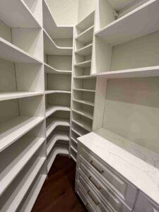 Custom white closet with floor-to-ceiling corner shelving, wraparound open shelves, and quartz drawer unit