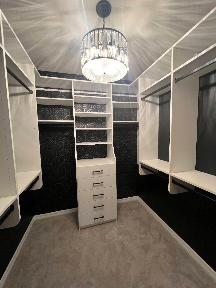 Large walk-in closet with white casework, frosted glass upper cabinet doors, full-length mirror, multi-drawer dresser tower, double hang rods, and accessory shelving